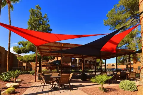 Red and dark shade sails above a landscaped dining patio.