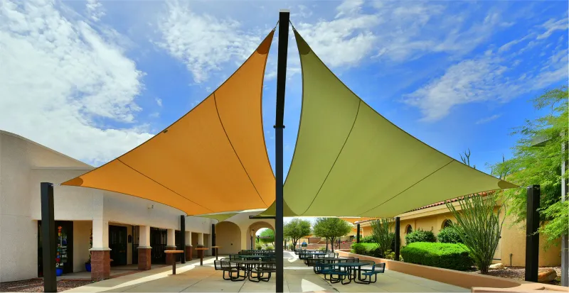Orange and green shade sails above courtyard tables, from SHADE Industries’ About page