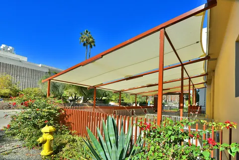 Long shade-panel structure beside landscaping and a walkway.