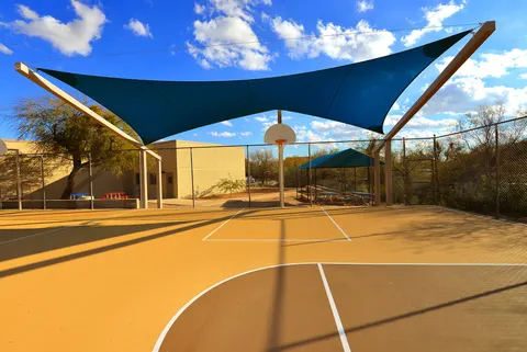 Dark triangular shade sail above a basketball court.
