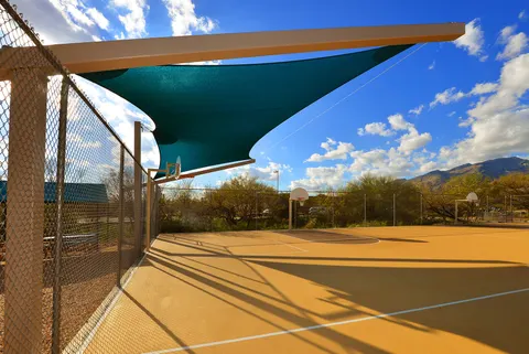 Shade sail above a fenced basketball court.