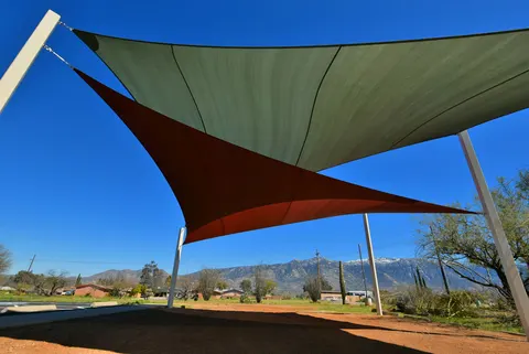 Overlapping light and red shade sails beside a building.