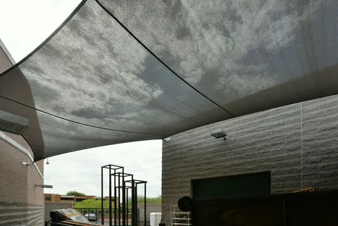 View beneath a dark shade sail between building walls.