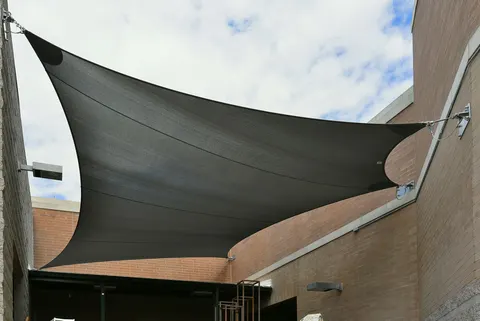 Layered shade sails spanning a building-side courtyard.