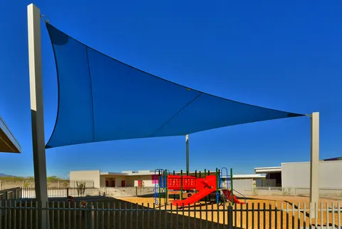 Blue shade sail above a fenced play area.