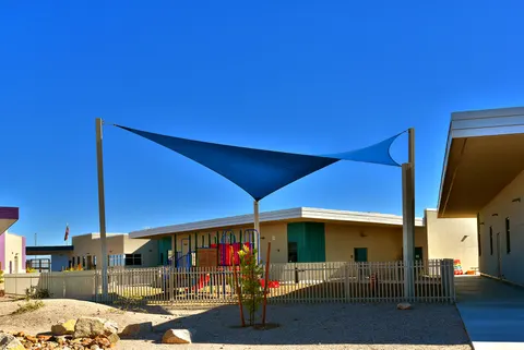 Blue shade sails beside a courtyard and play equipment.