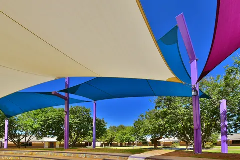 Layered shade sails above a path and landscaped seating area.