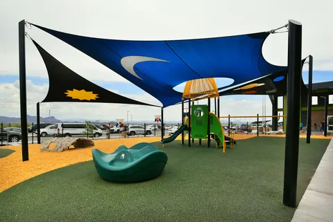 Blue patterned shade sail above climbing and play equipment.