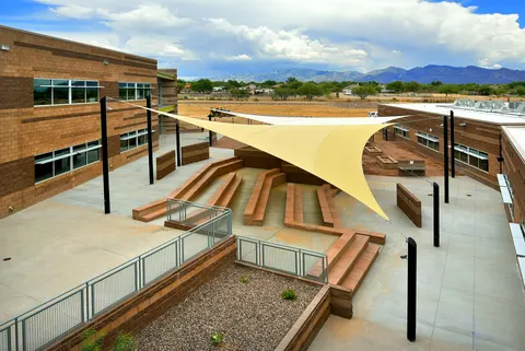 Light-colored shade sail above stepped courtyard seating.