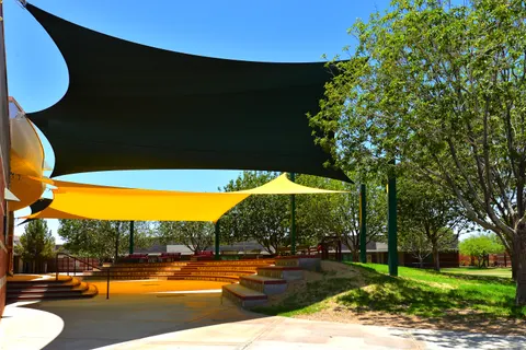 Shade sails spanning stepped outdoor seating beside trees.
