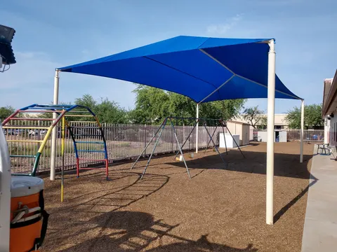 Blue shade sails above fenced playground equipment.