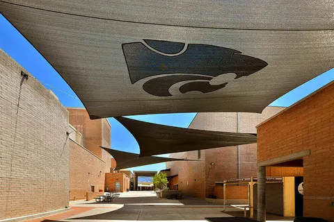 Shade sail with a visible emblem above a courtyard walkway.