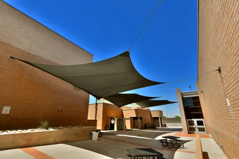 Dark shade sails above tables between campus buildings.
