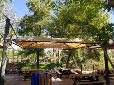 Light-colored framed canopy above tables among trees.