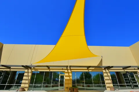 Upward view of yellow shade fabric beside a building.