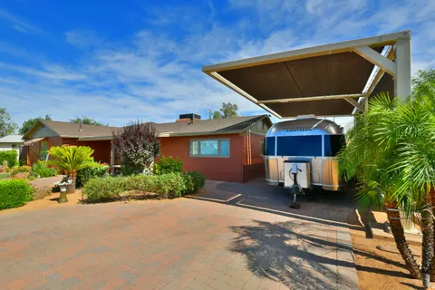 Framed canopy above a travel trailer beside a residence.