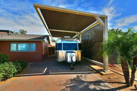 Front view of a canopy and travel trailer beside a residence.