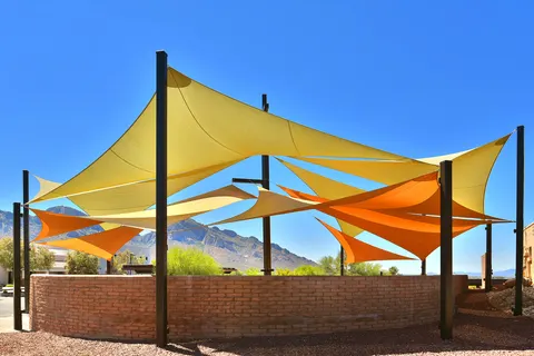 Overlapping yellow and orange sails above a fenced outdoor area.