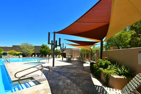Shade sails beside a pool and outdoor lounge chairs.
