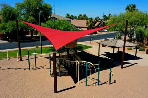 Red shade sails above playground equipment and outdoor tables.