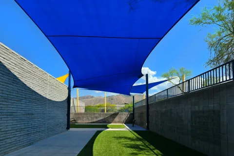 Blue shade sail above a narrow courtyard and lawn.