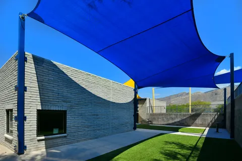 Blue shade sails spanning a landscaped building-side courtyard.