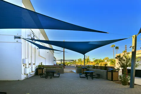 Blue shade sails above outdoor tables beside a building.