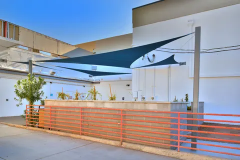 Blue shade sails above a fenced dining patio.