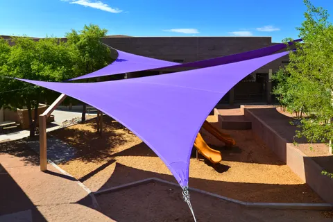 Purple triangular shade sail above a fenced playground.